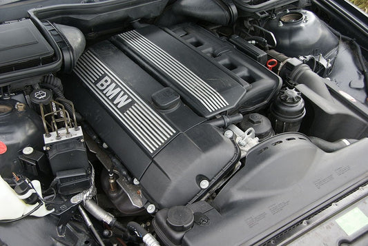 BMW M54 inline-six engine, displayed in a clean engine bay. The engine features prominent BMW branding and showcases its intricate design and engineering, known for its smooth performance and reliability.