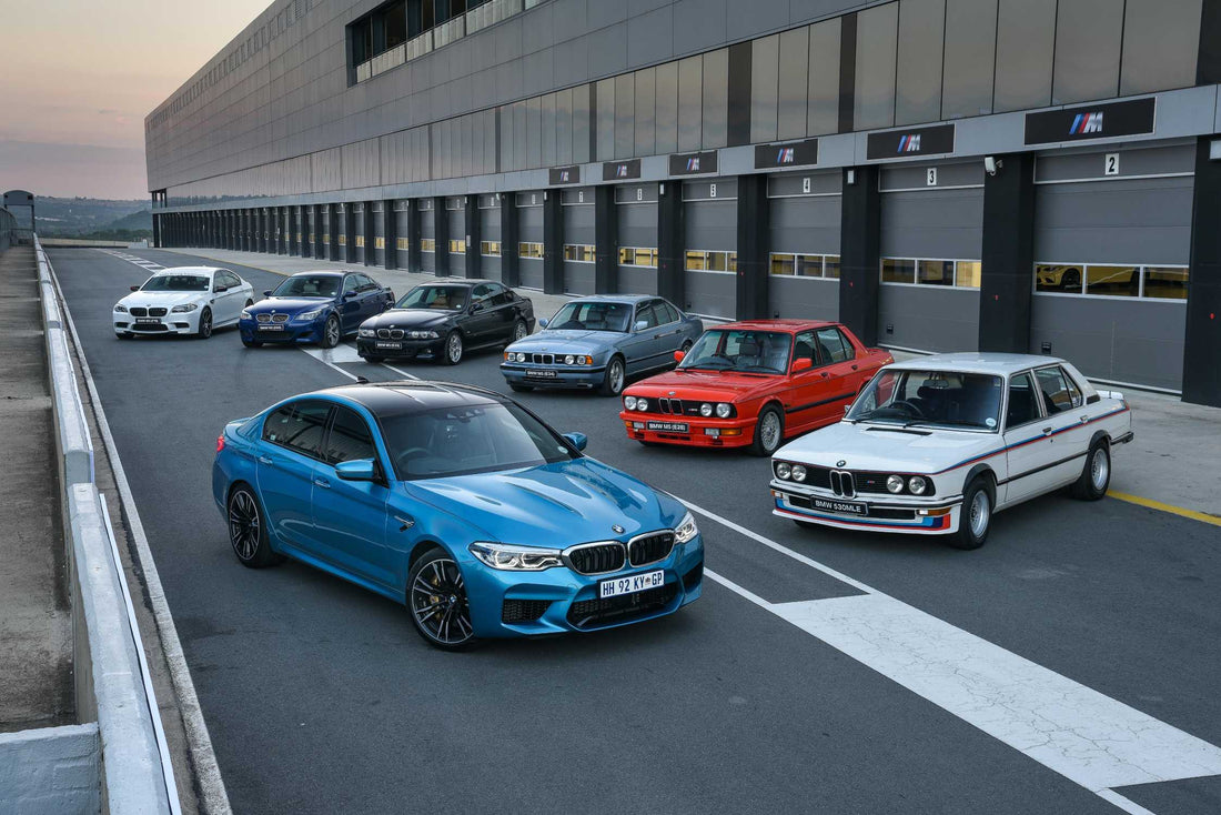 Lineup of all BMW M5 generations parked together, showcasing the evolution from the classic E28 to the modern G90 hybrid, highlighting their design changes. Bavarian old school