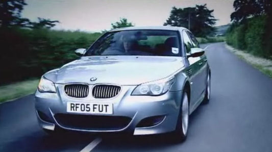 A BMW E60 M5 V10 driving on the road, showcasing its sleek design and powerful presence with a scenic backdrop. bavarian old school