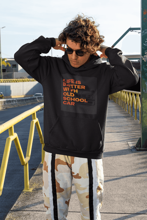Person wearing a black hoodie with text Life is better with old school car and graphics BMW e30 with camouflage pants on a sidewalk. Bavarian old school
