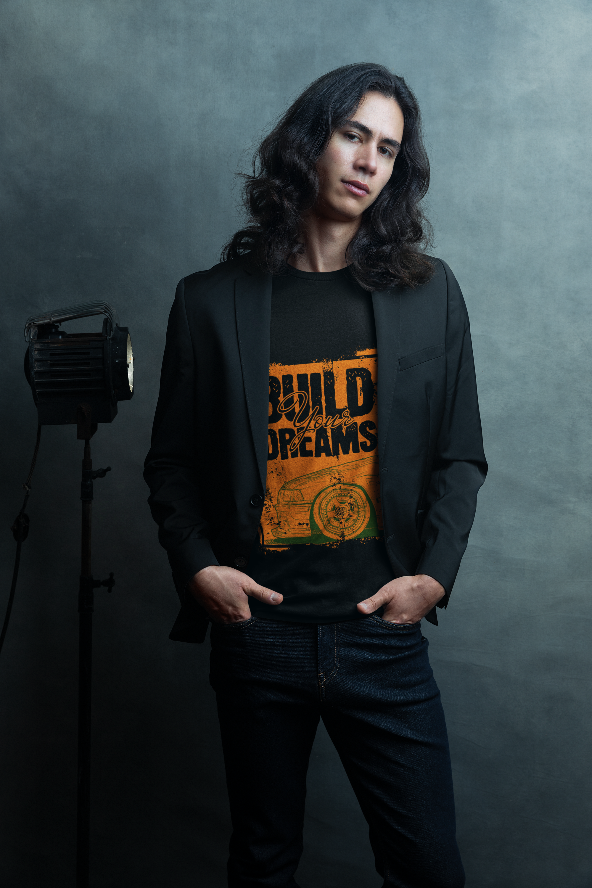 Person wearing a black blazer over an orange graphic t-shirt with text and design, standing against a dark background.