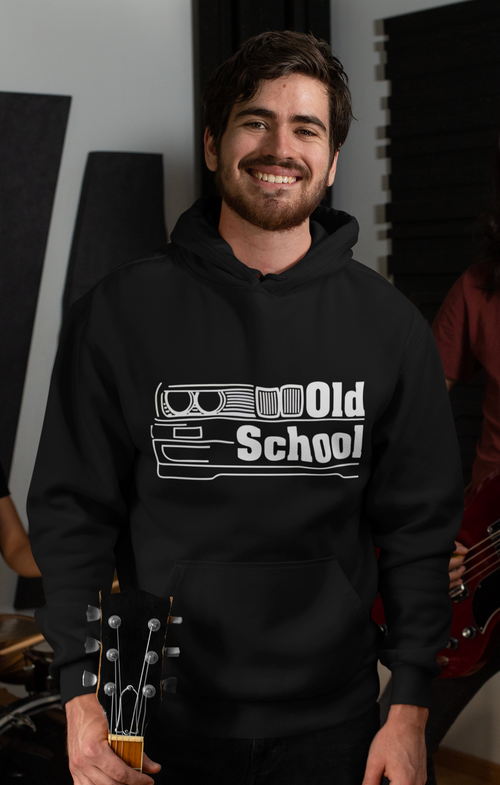 Man wearing a black hoodie with 'Old School' design, holding a guitar in a room with musical equipment.
