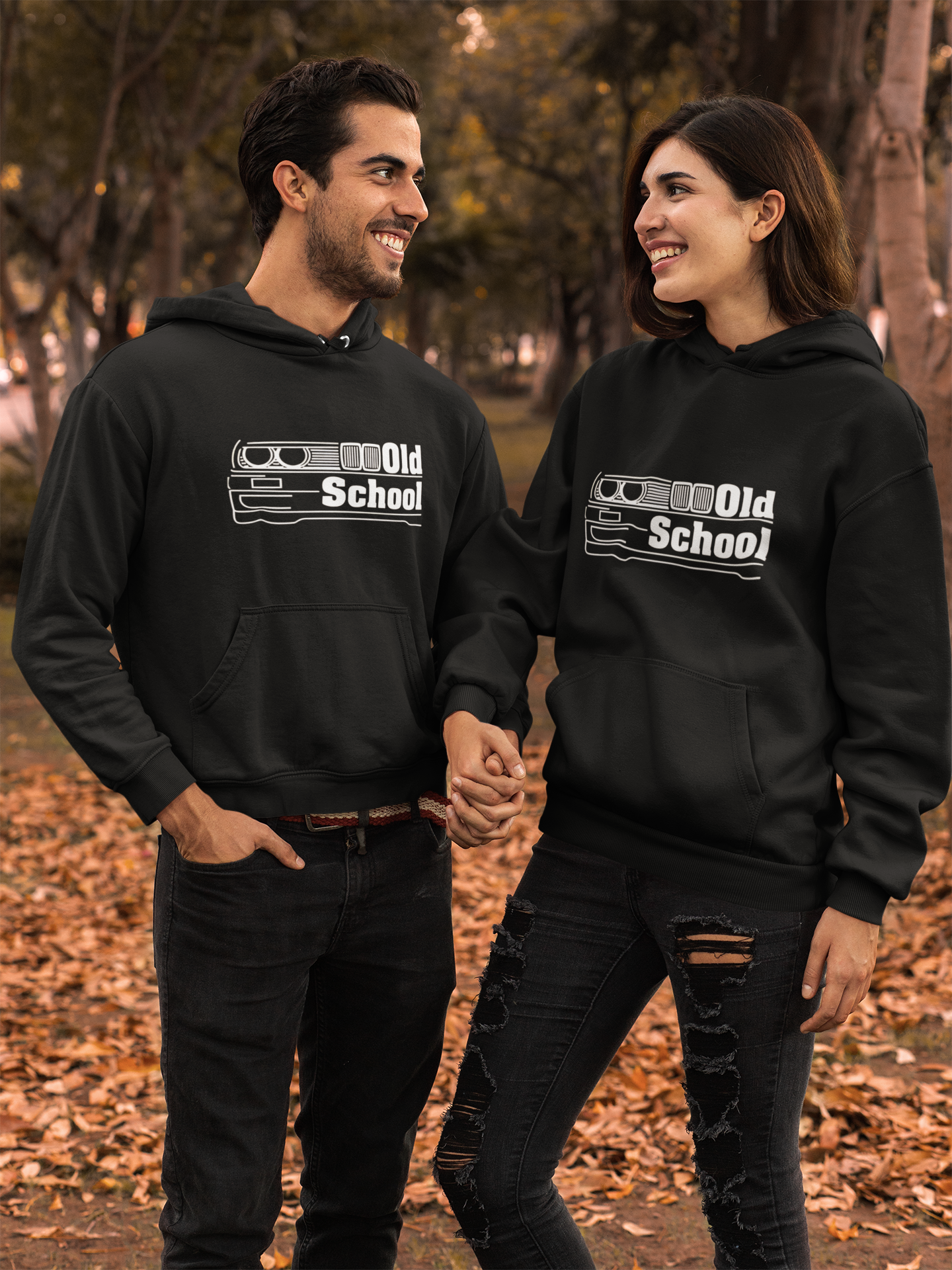 Two people wearing black hoodies with 'Old School' design in a park setting.
