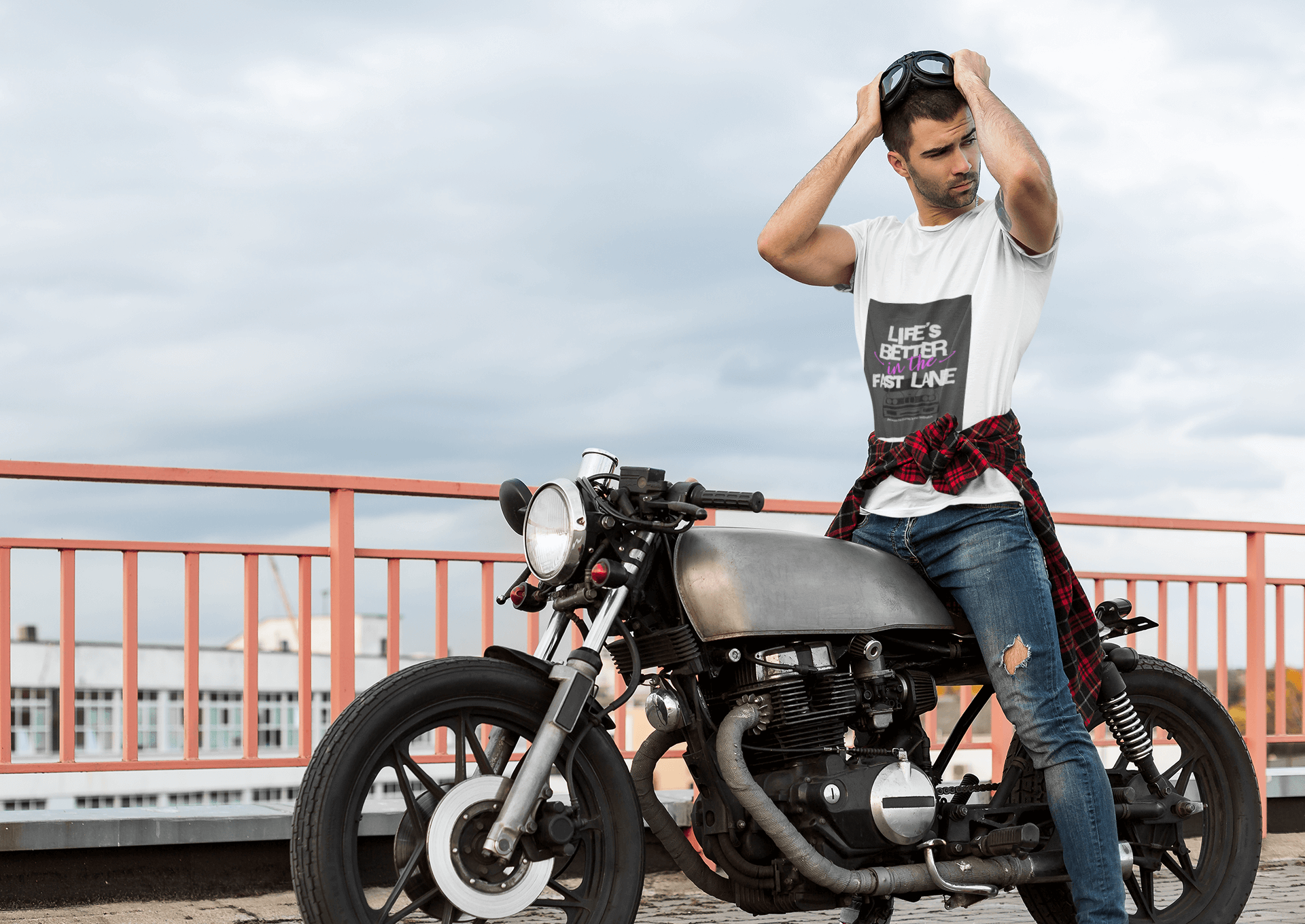 Man posing with a motorcycle on a bridge wearing tee with text Life`s better in the fast lane. Bavarian old school