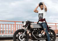 Man posing with a motorcycle on a bridge wearing tee with text Life`s better in the fast lane. Bavarian old school