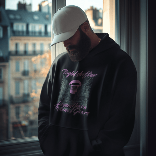 Person wearing a black hoodie with text and graphics, standing by a window with cityscape view.